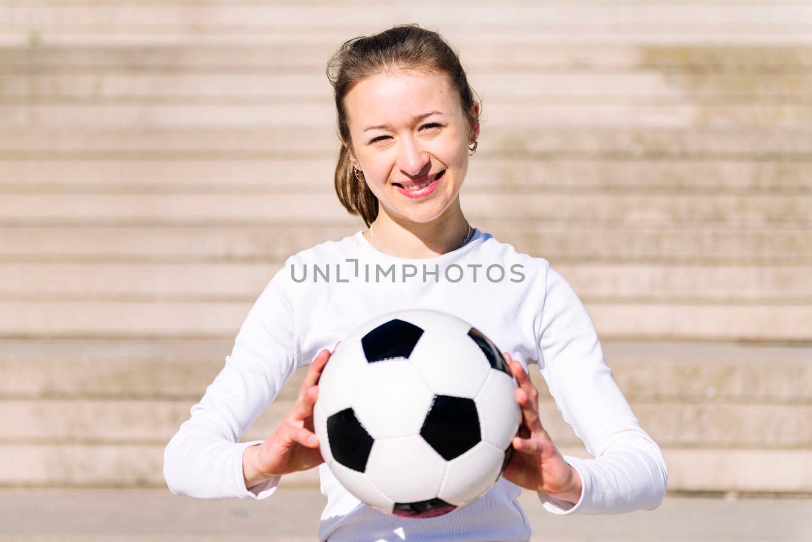 portrait of a smiling sports woman in a concrete soccer court with a ball in her hands, concept of football lifestyle and urban sport in the city