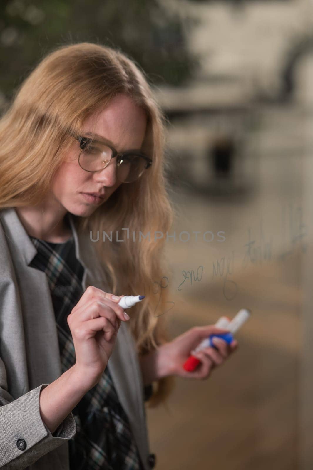 Caucasian woman with glasses writes text in English on a glass wall