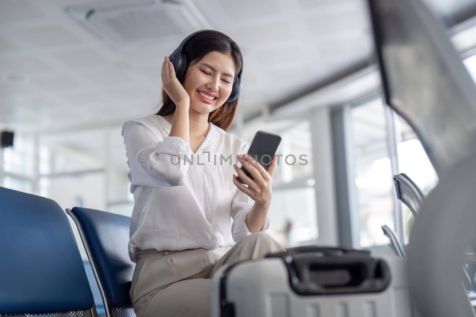 Businesswoman Traveler at Modern Airport Terminal Using Smartphone and Headphones While Waiting for Flight by nateemee