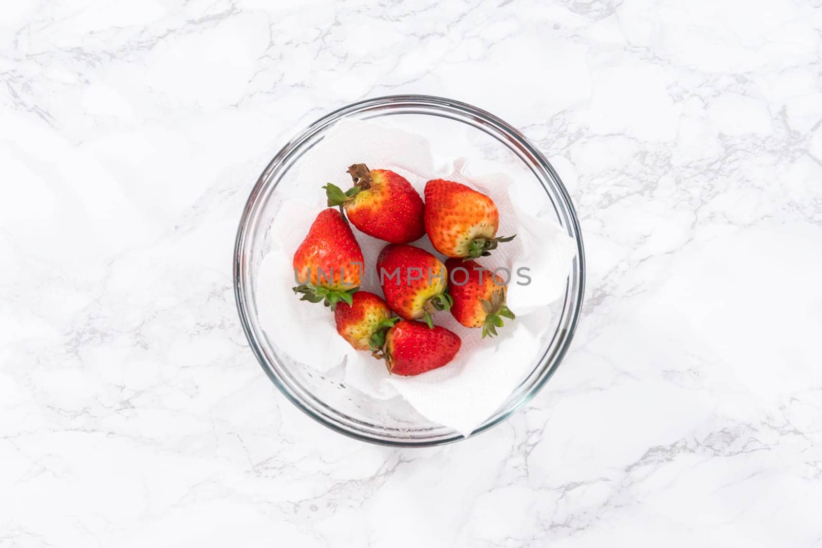 Freshly washed and dried strawberries are carefully arranged in a glass bowl lined with paper towel, ready for snacking or further use.