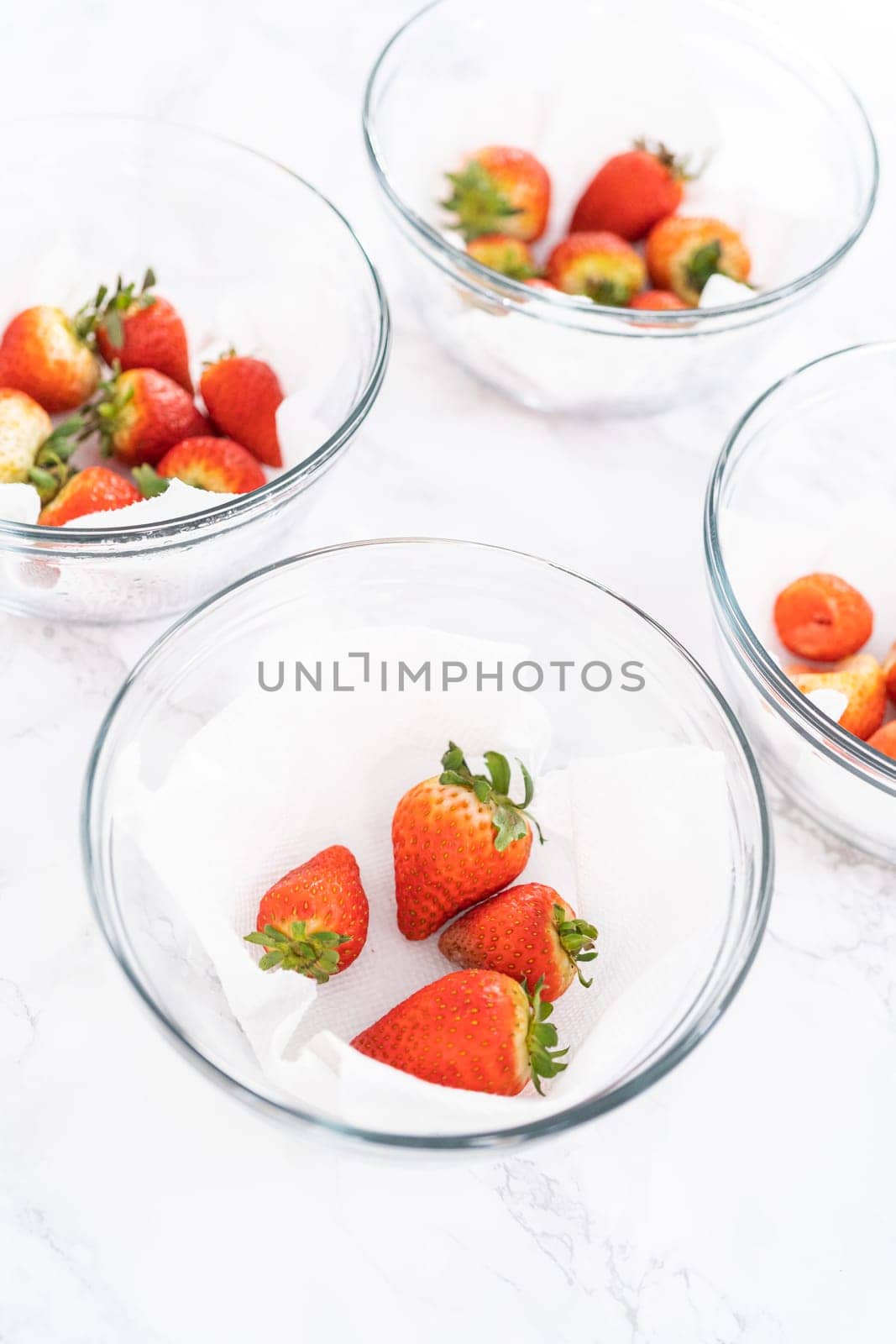 Freshly washed and dried strawberries are carefully arranged in a glass bowl lined with paper towel, ready for snacking or further use.