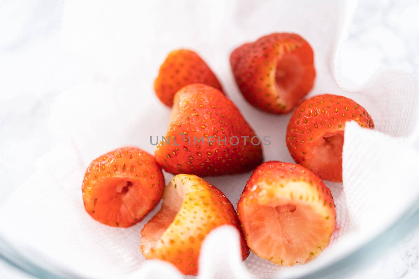 Freshly washed and dried strawberries are carefully arranged in a glass bowl lined with paper towel, ready for snacking or further use.