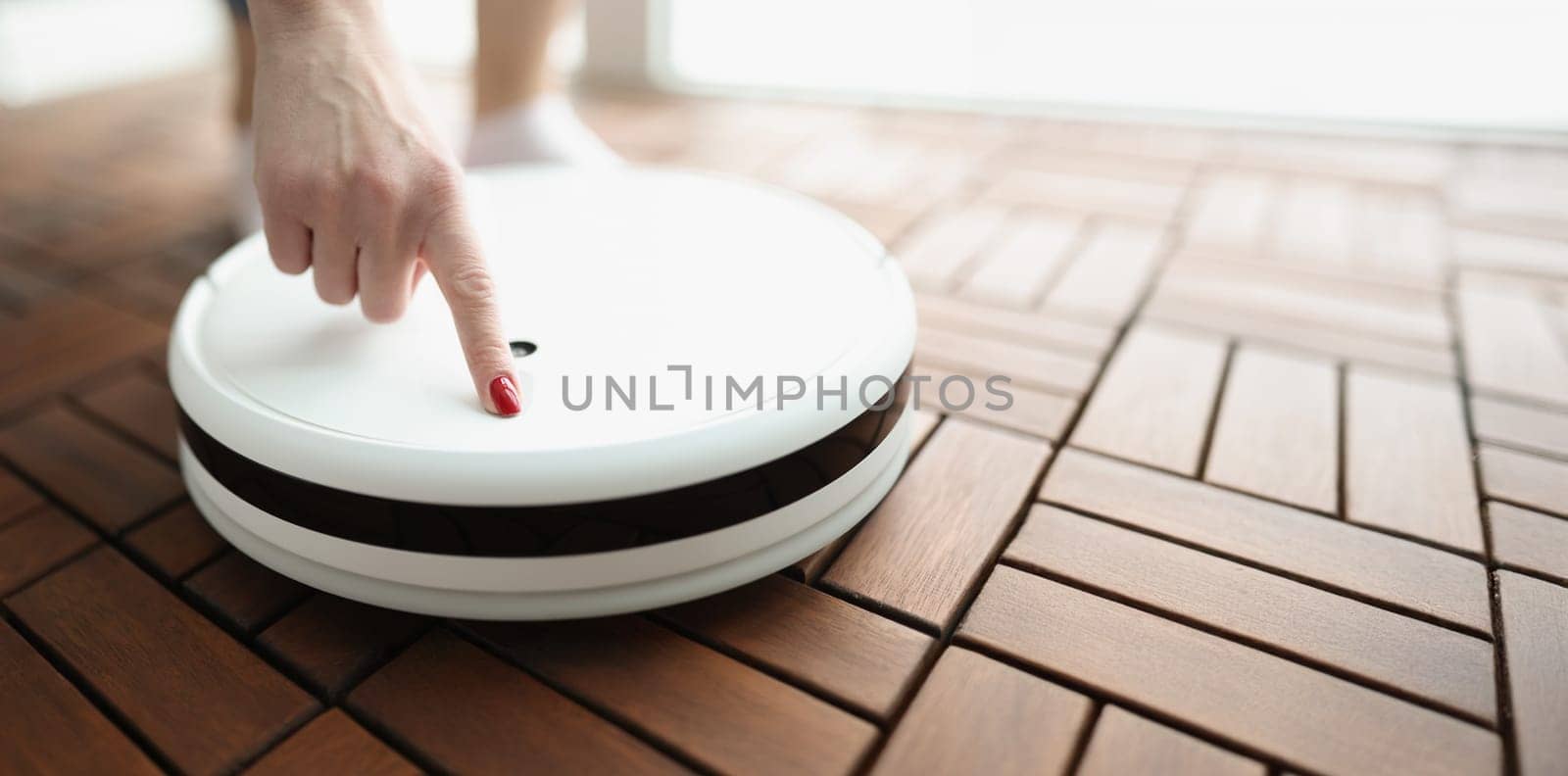 Female finger presses power button on white robotic vacuum cleaner. Home cleaning appliances concept