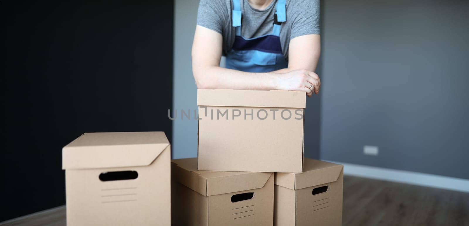 Man in overalls putting his hands on cardboard boxes closeup. Moving assistance concept