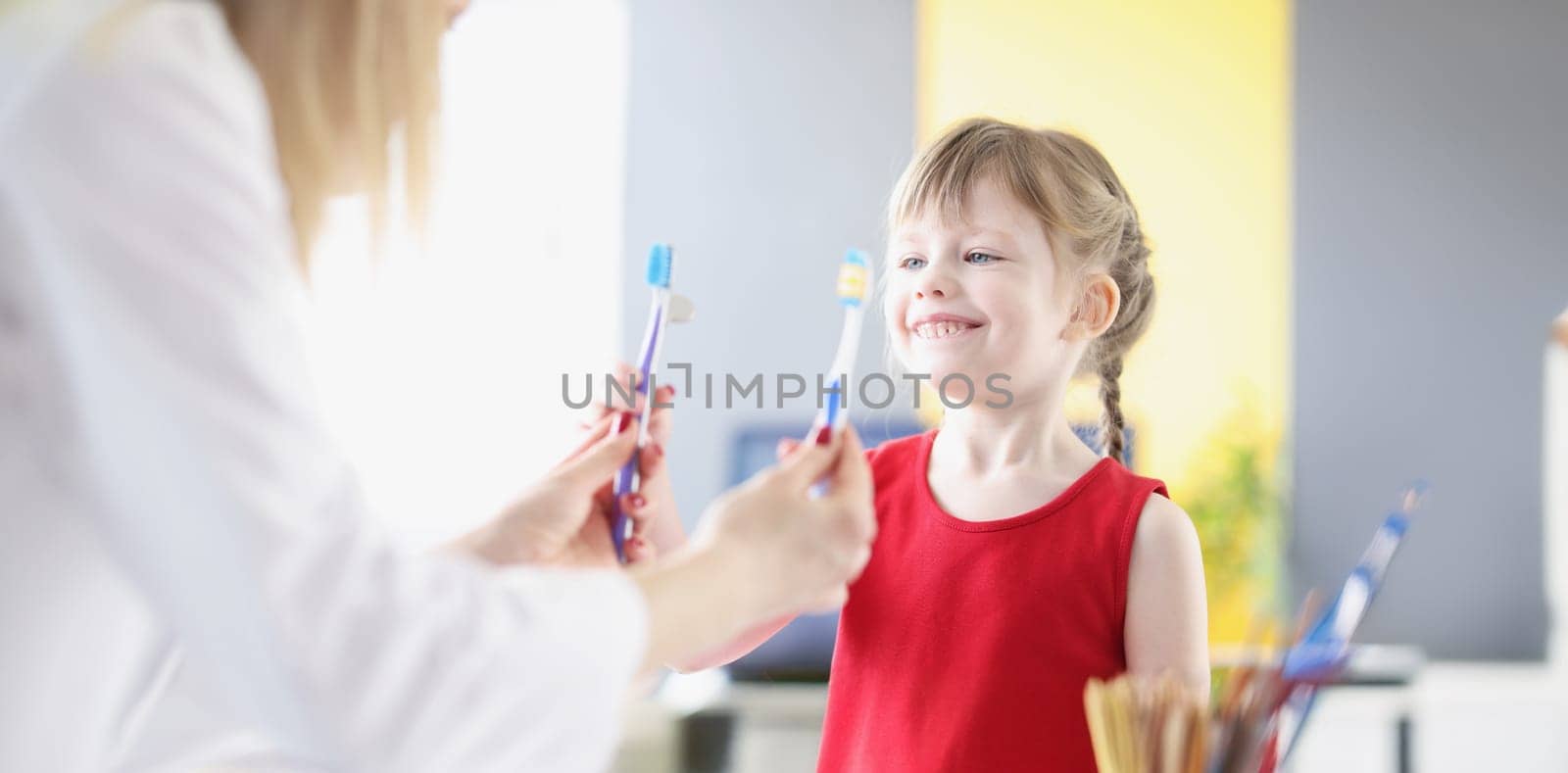 Little girl choosing toothbrush at dentist in clinic by kuprevich