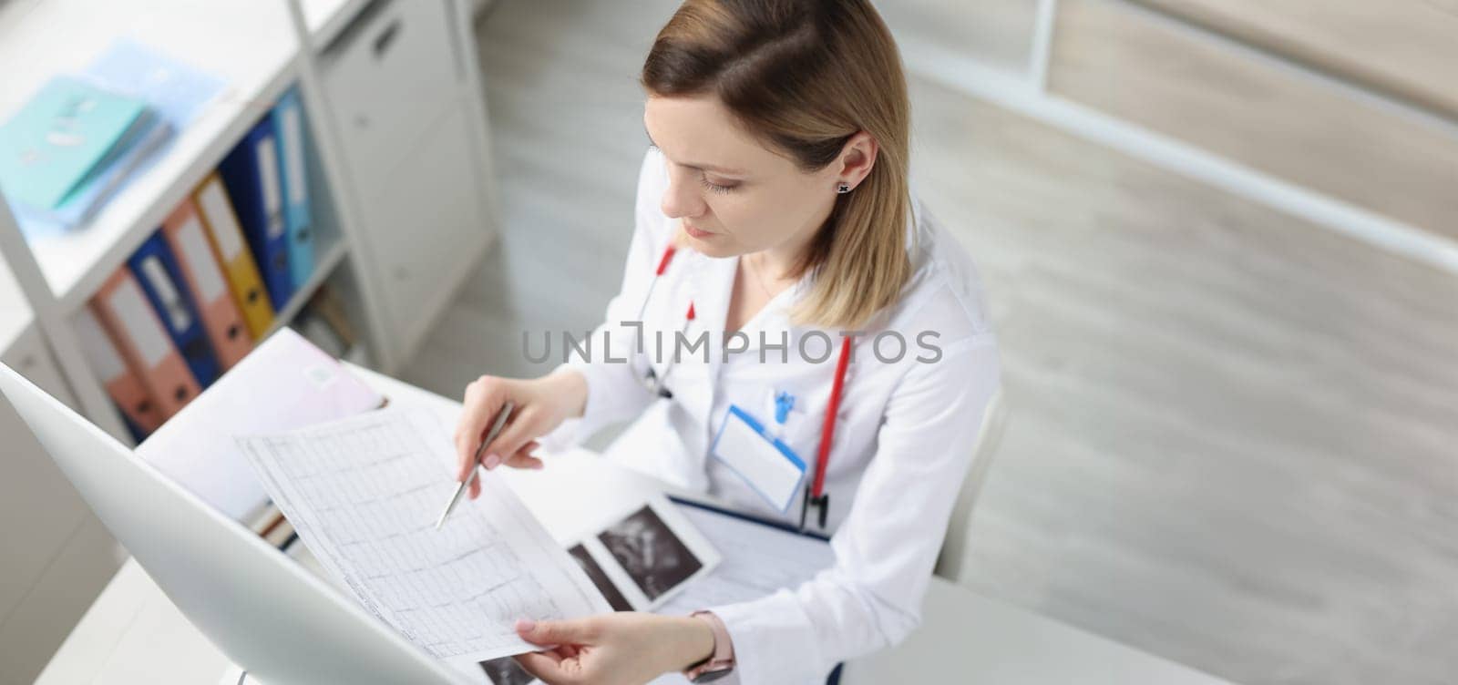 Doctor sitting at table and looking at cardiogram in clinic. Diagnostics and treatment of angina pectoris myocardial infarction concept