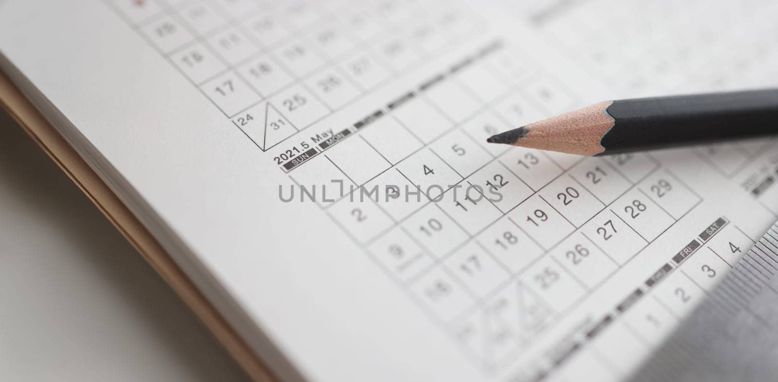 Sharp black pencil lying on calendar closeup. Scheduling action concept