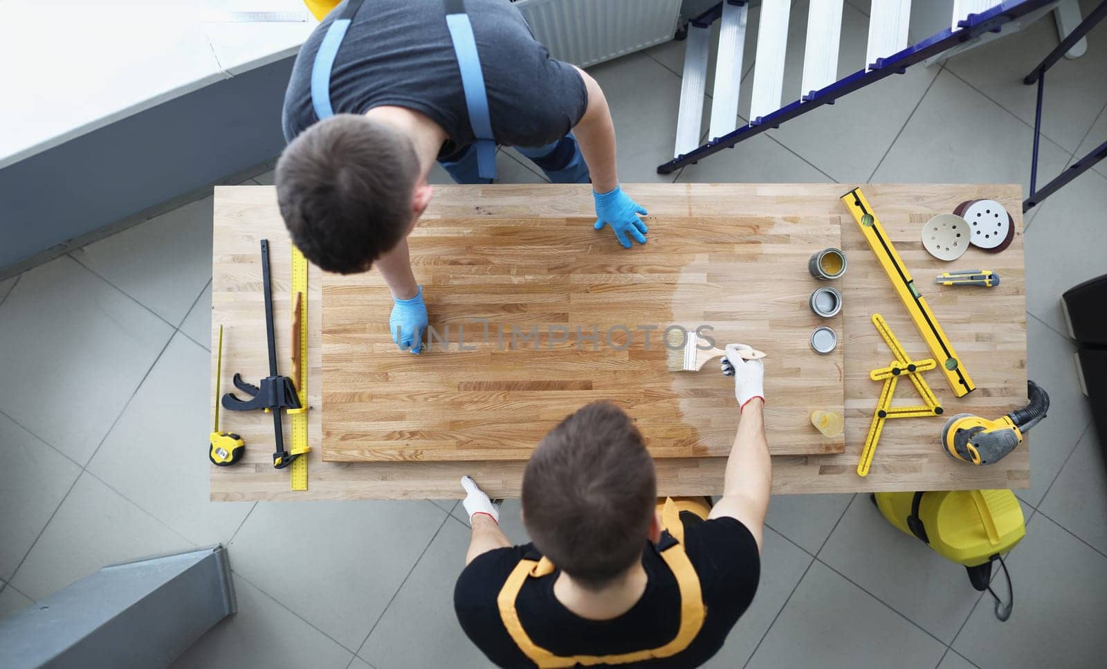 Two male construction workers are covering wood floor with protective layer of varnish. Processing of wooden products concept