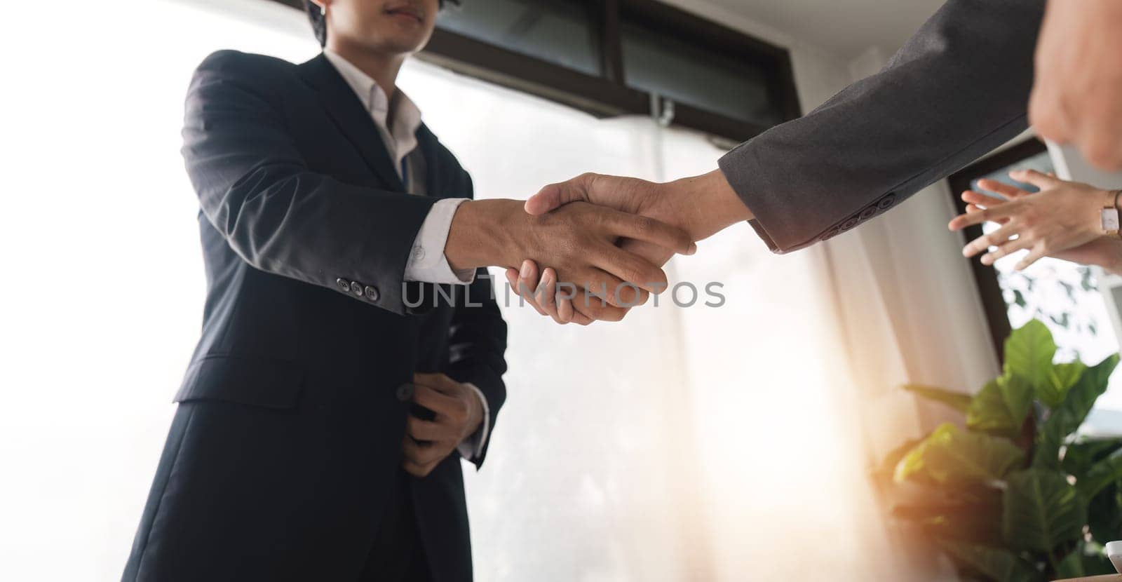 Businessmen Shaking Hands in Modern Office Setting, Sealing a Deal and Making Agreements Together by wichayada