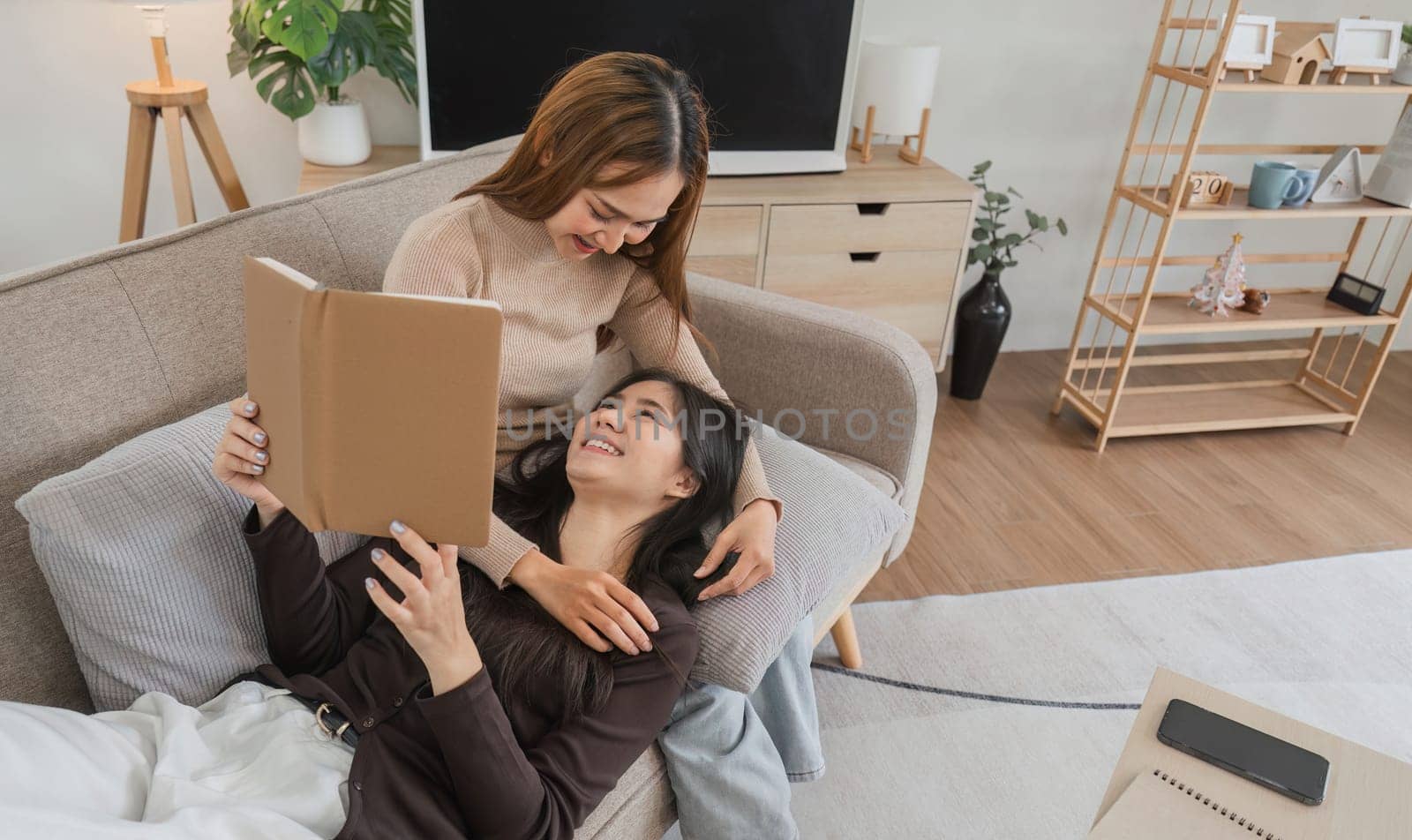 Happy lesbian couple sitting together in a cozy living room, sharing a moment of relaxation and bonding over a book.