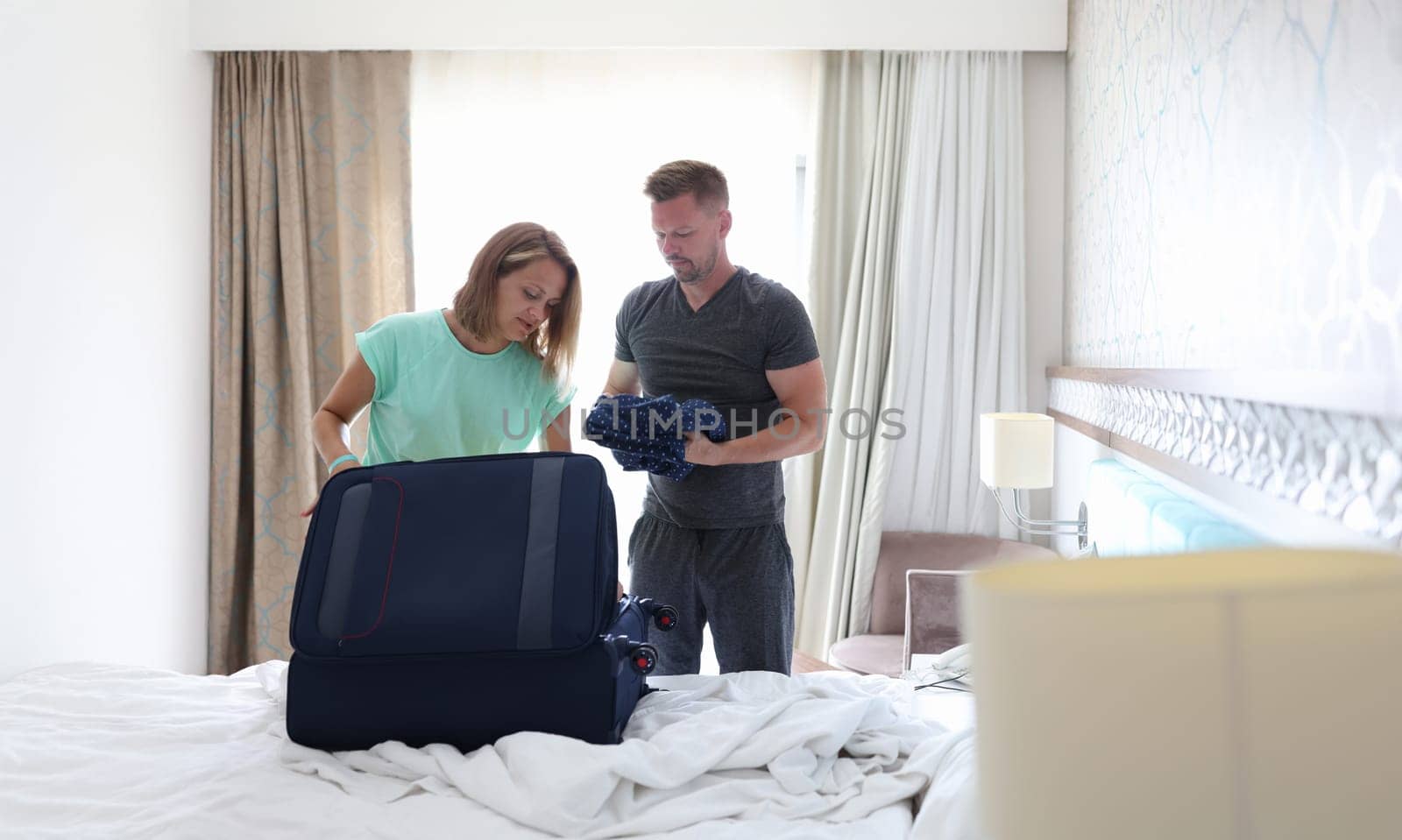 Man and woman are putting things in suitcase in bedroom. Work trip and travel concept