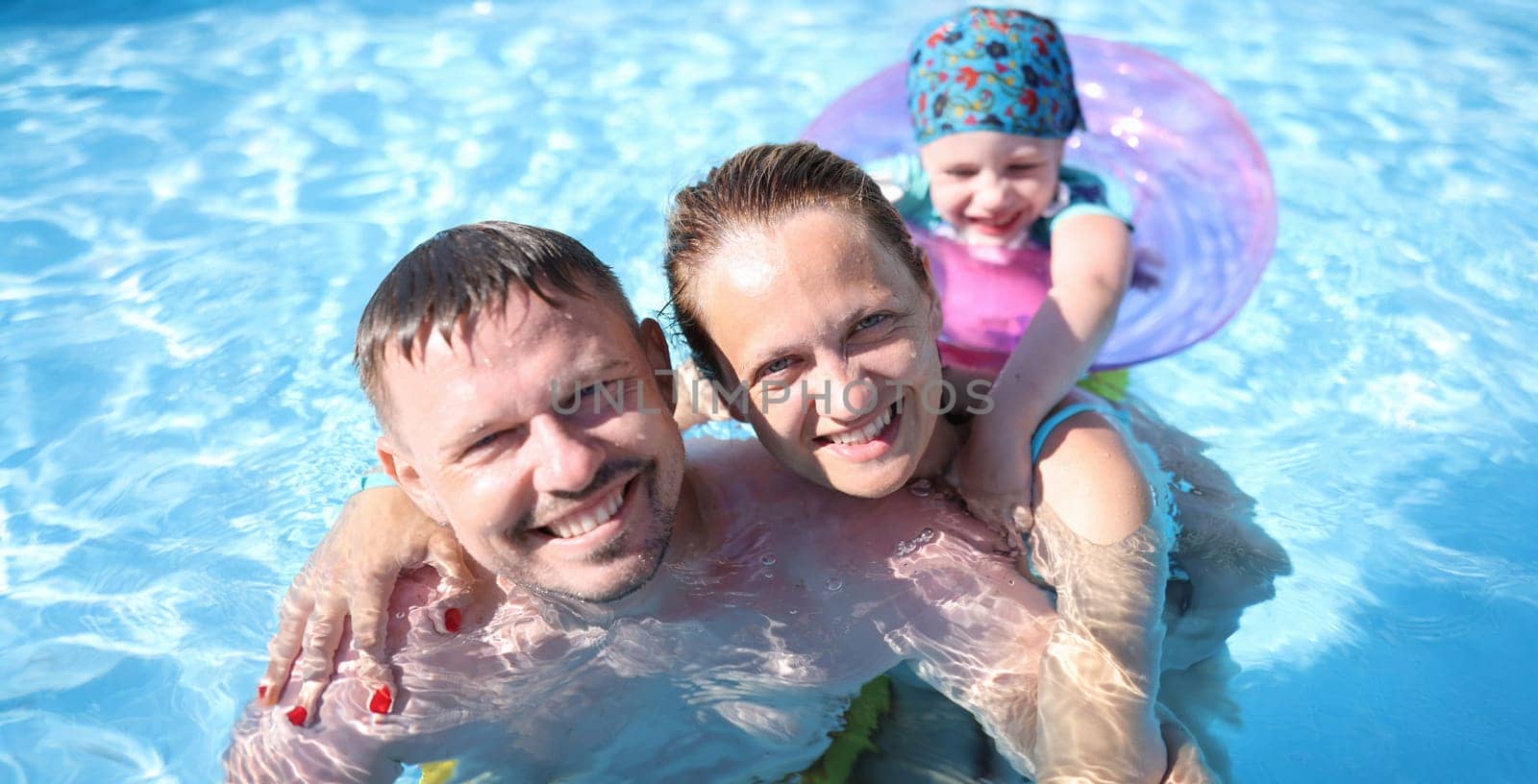 Family portrait of smiling parents and child in pool. Family swimming for kids and adults concept