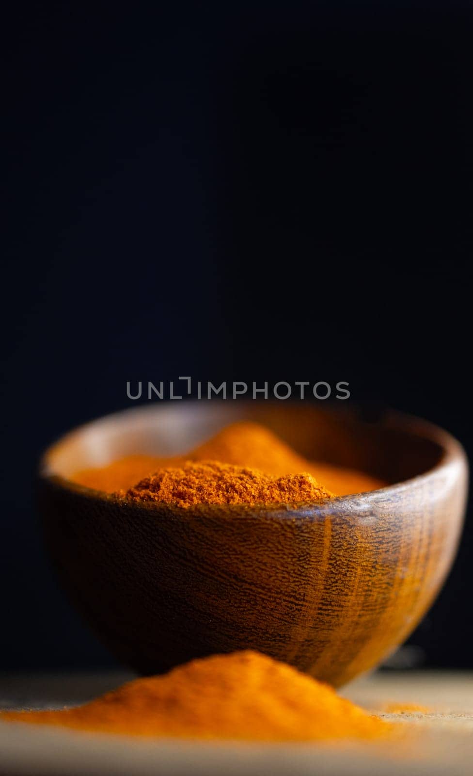 Vertical close up view of red paprika powder on a wooden bowl by VeroDibe