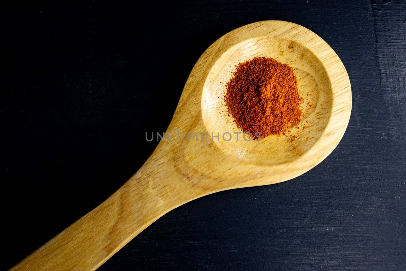 Top view of red paprika on a wooden spoon on black background by VeroDibe