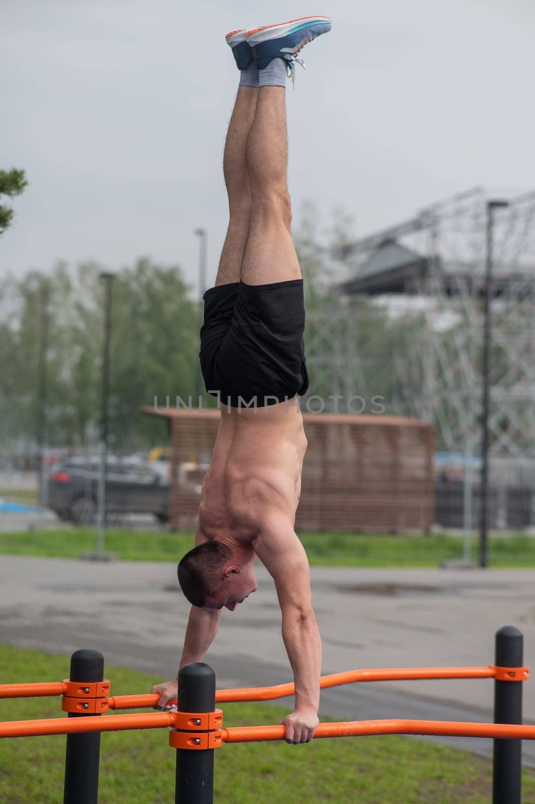 A young man doing a handstand on parallel bars outdoors. Workout