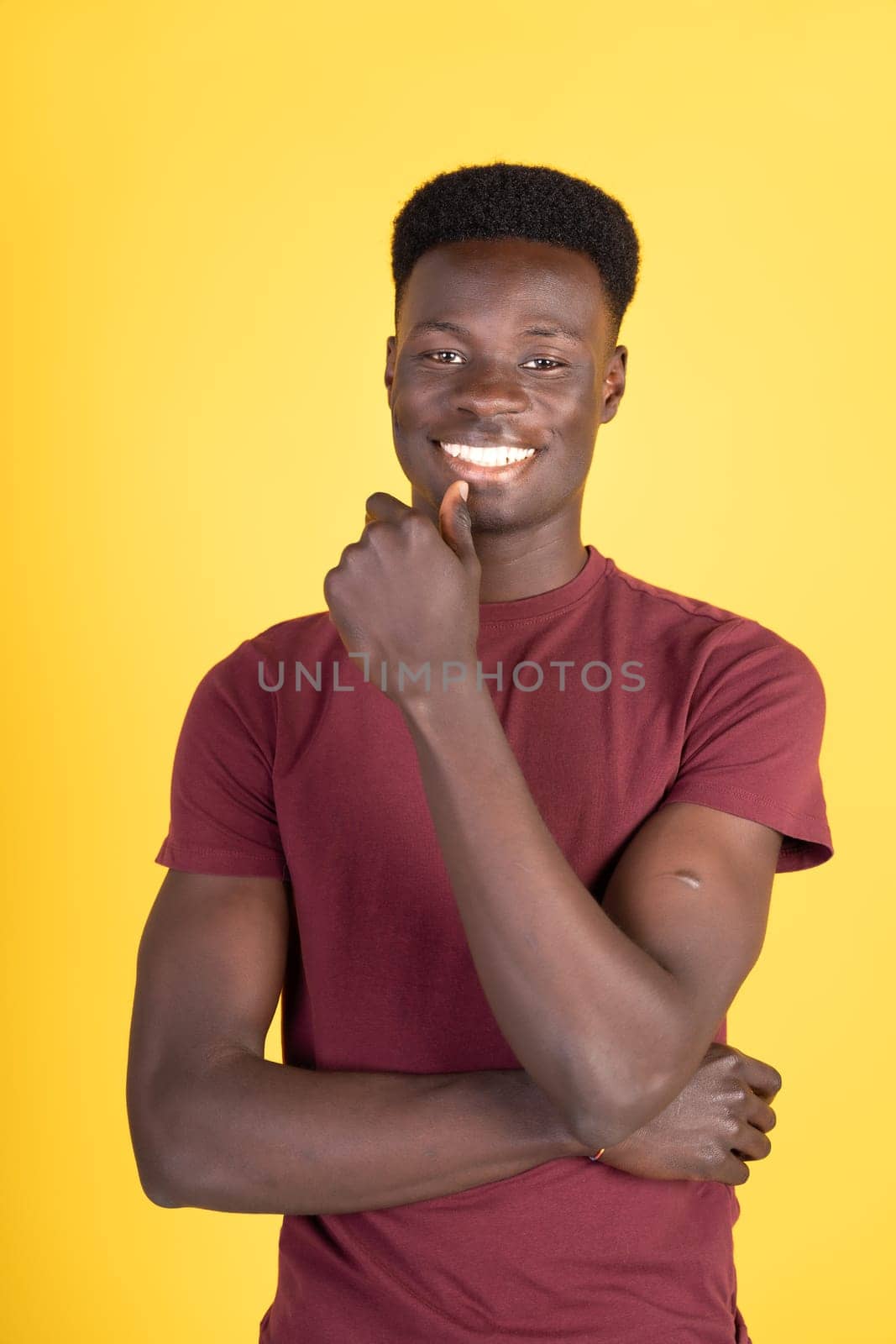 A young man in a red shirt is posing for a picture with his hands crossed. He has a smile on his face and he is thinking