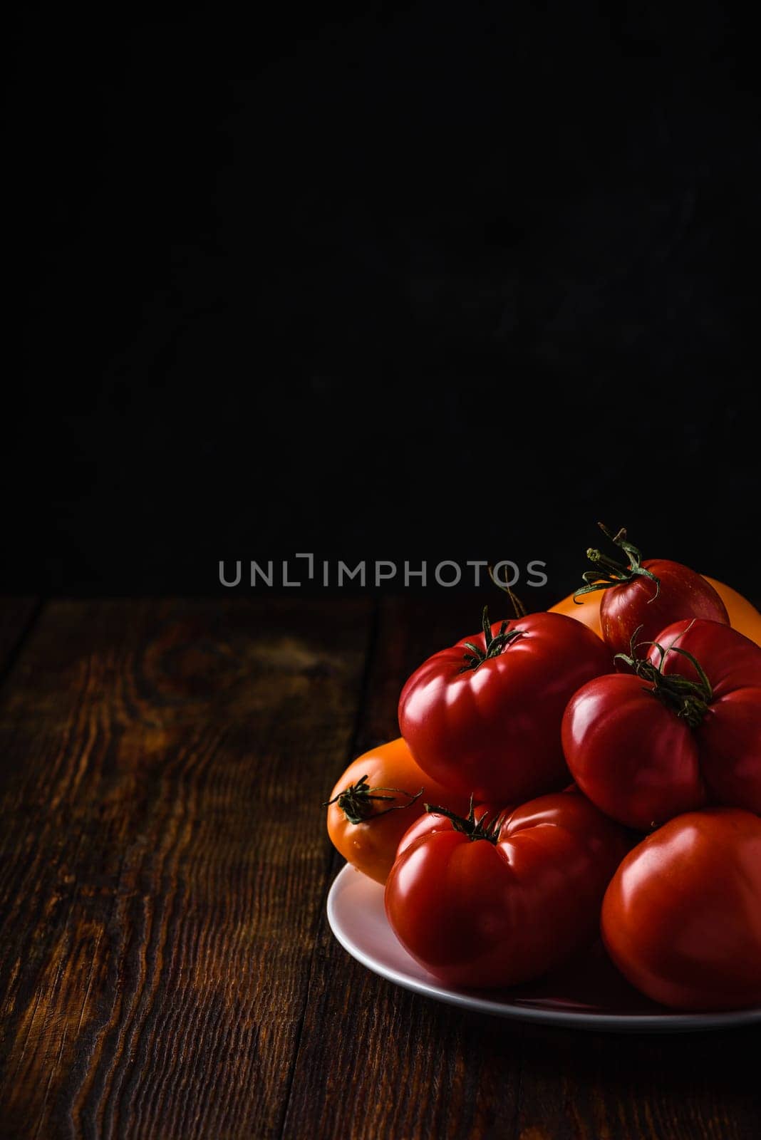 Fresh red and yellow tomatoes on white plate over wooden surface