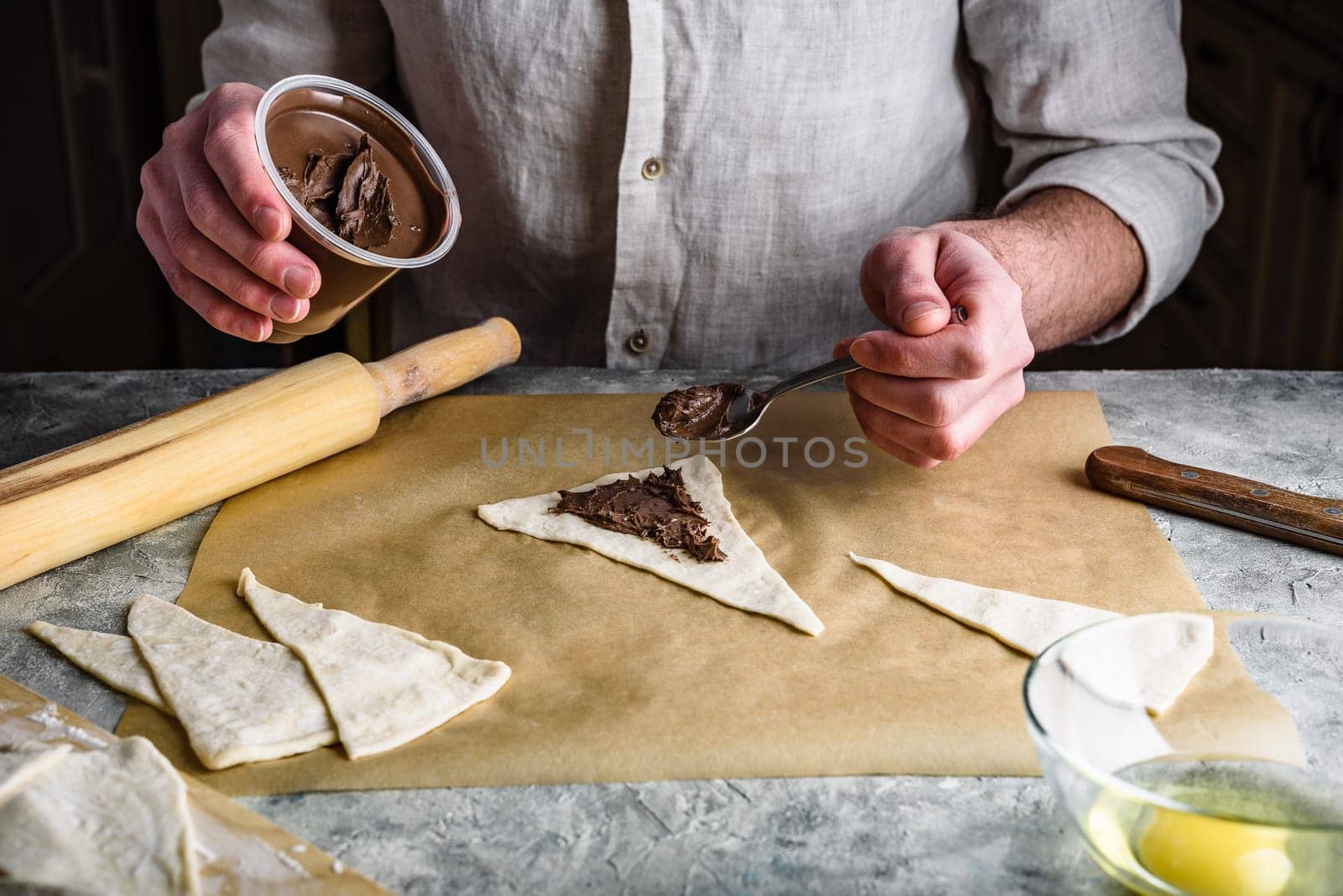 Homemade croissant preparing. Baker distributes hazelnut spread among puff pastry triangles