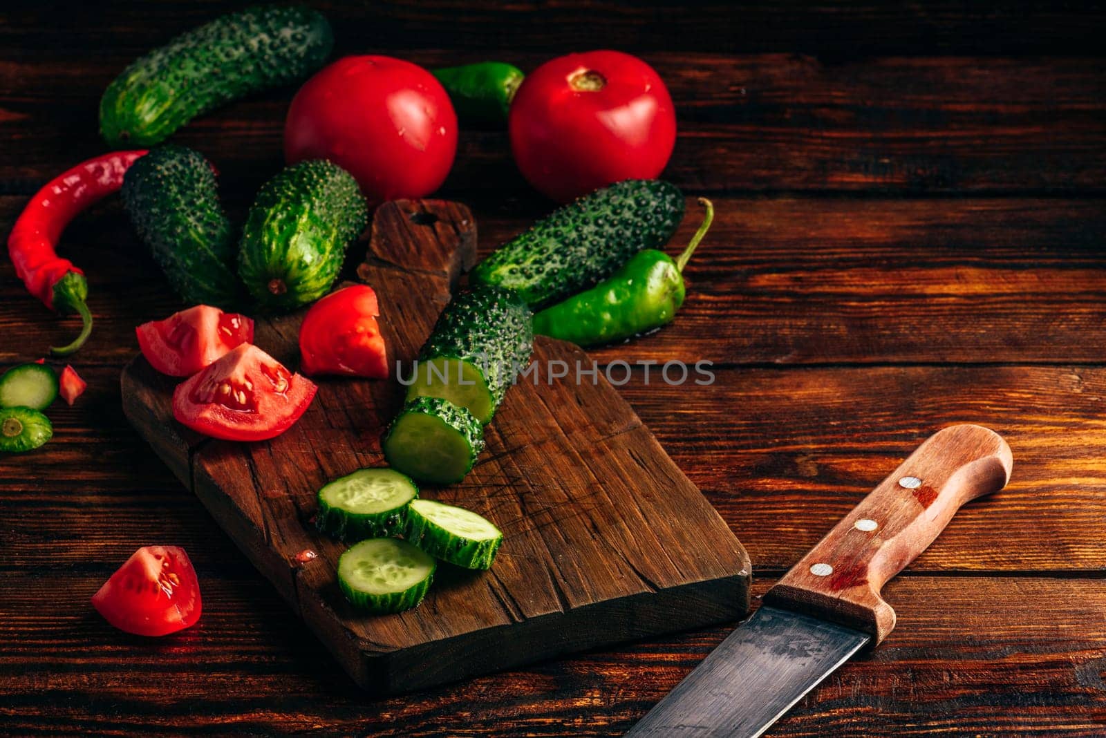 Sliced vegetables. Tomatoes, cucumbers and chili peppers over wooden background.