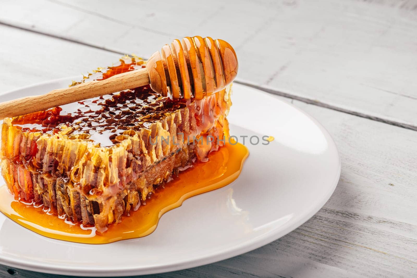 Delicious honeycomb on white plate with wooden honey dipper