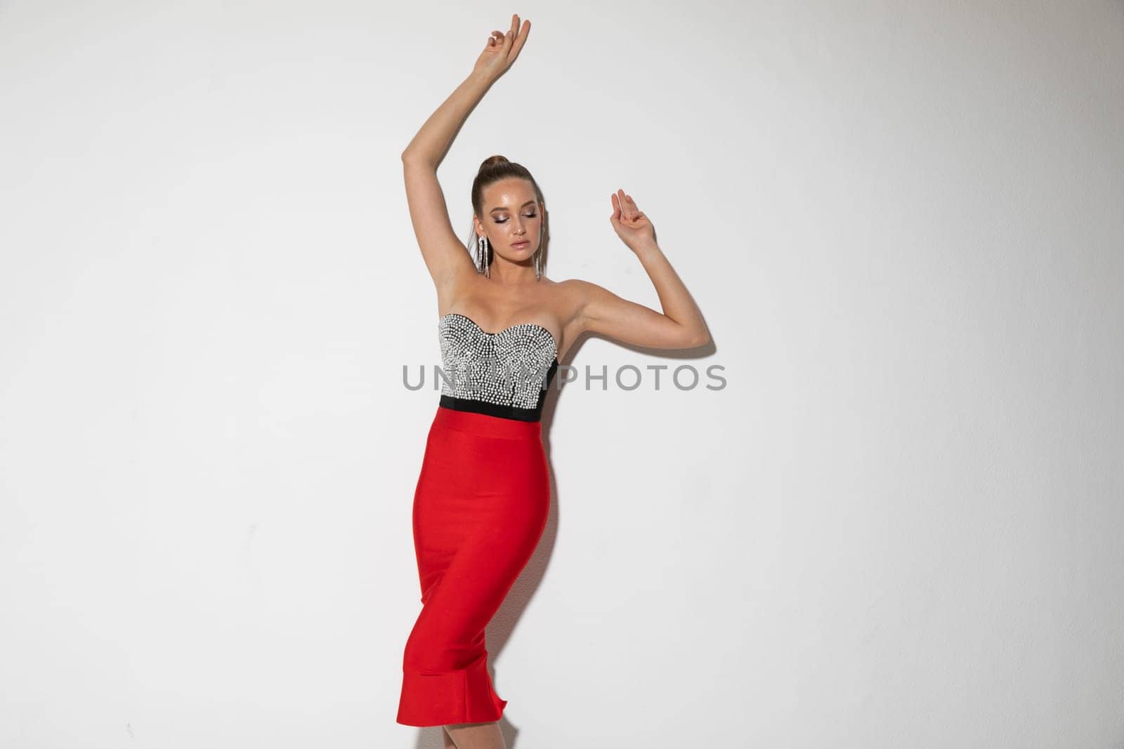 an elegant woman in beautiful clothes stands against white wall