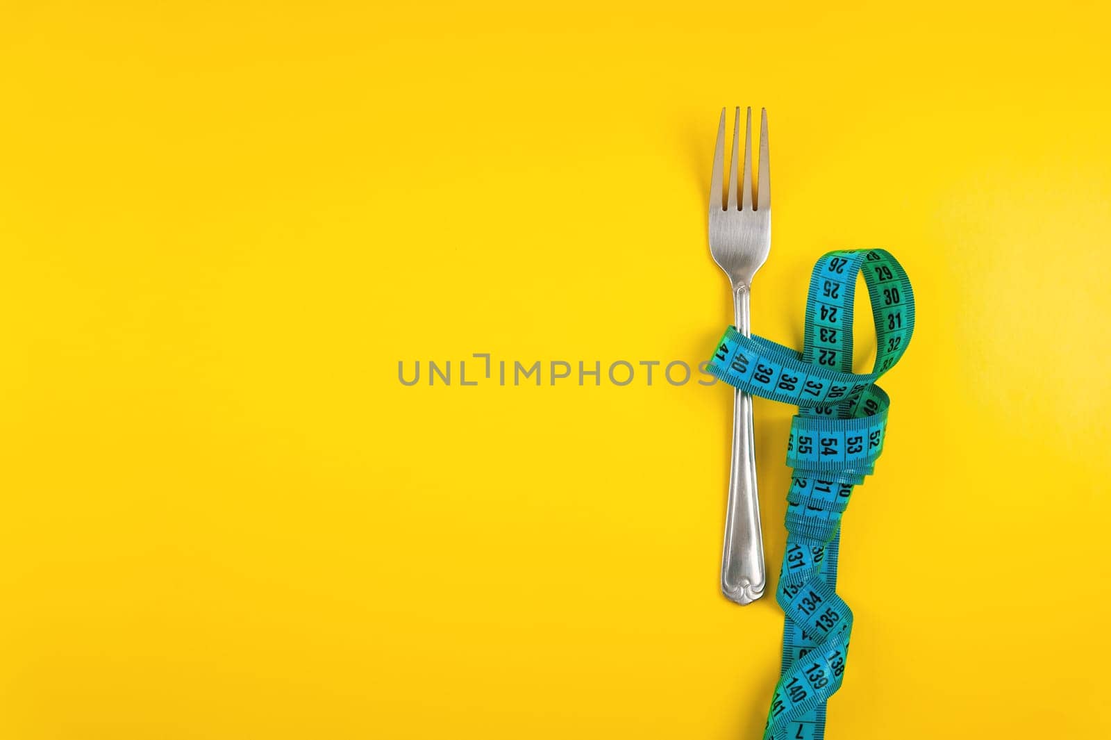 Diet, weight loss and weight loss concept. Fork with measuring tape on yellow background, top view, space for text.