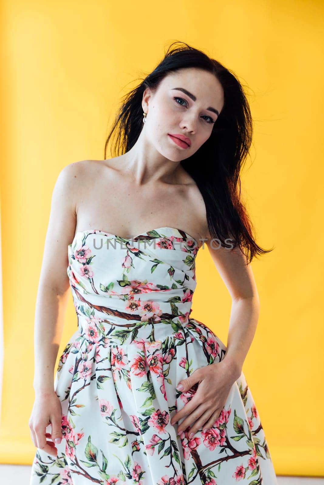 brunette woman in a floral dress posing on a yellow background