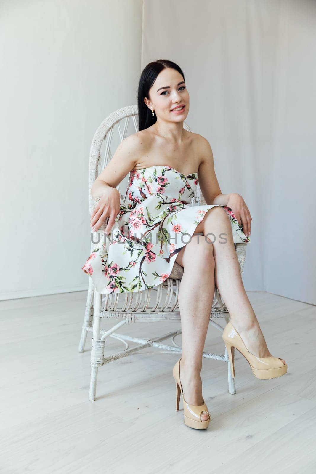 beautiful woman in a floral dress sits in a chair in a bright room