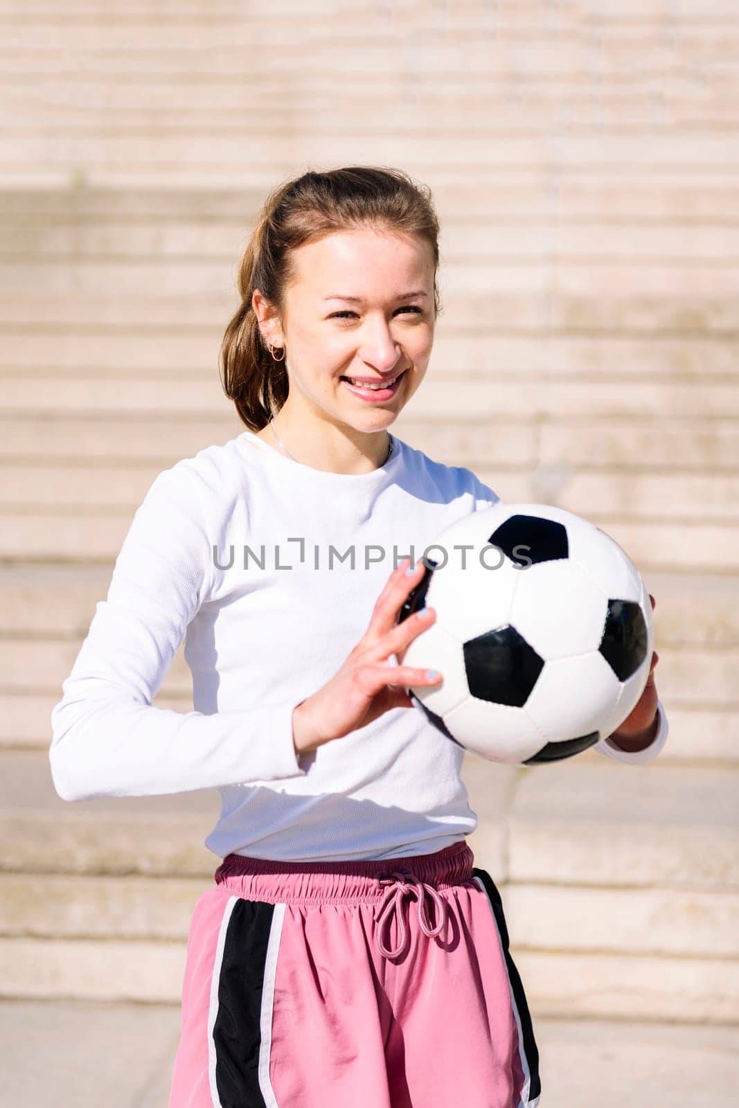 portrait of a smiling sports woman in a concrete soccer court with a ball in her hands, concept of football lifestyle and urban sport in the city