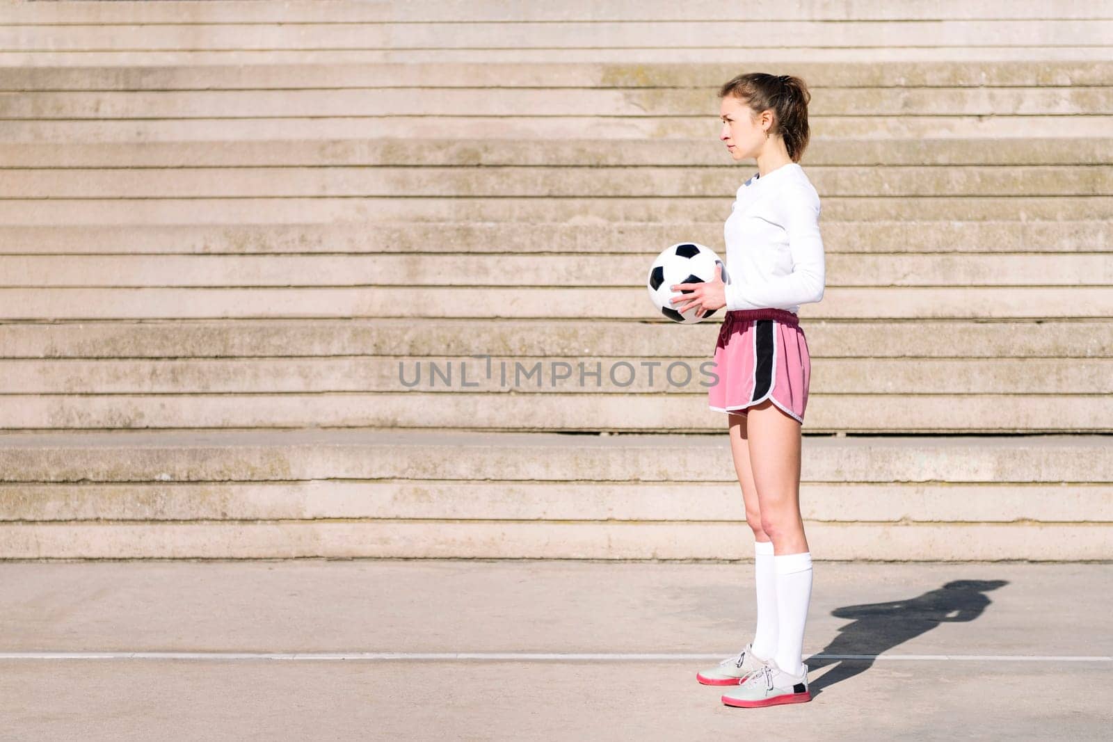 caucasian sports woman standing with the ball in her hand on a concrete soccer court, concept of football lifestyle and urban sport in the city, copy space for text