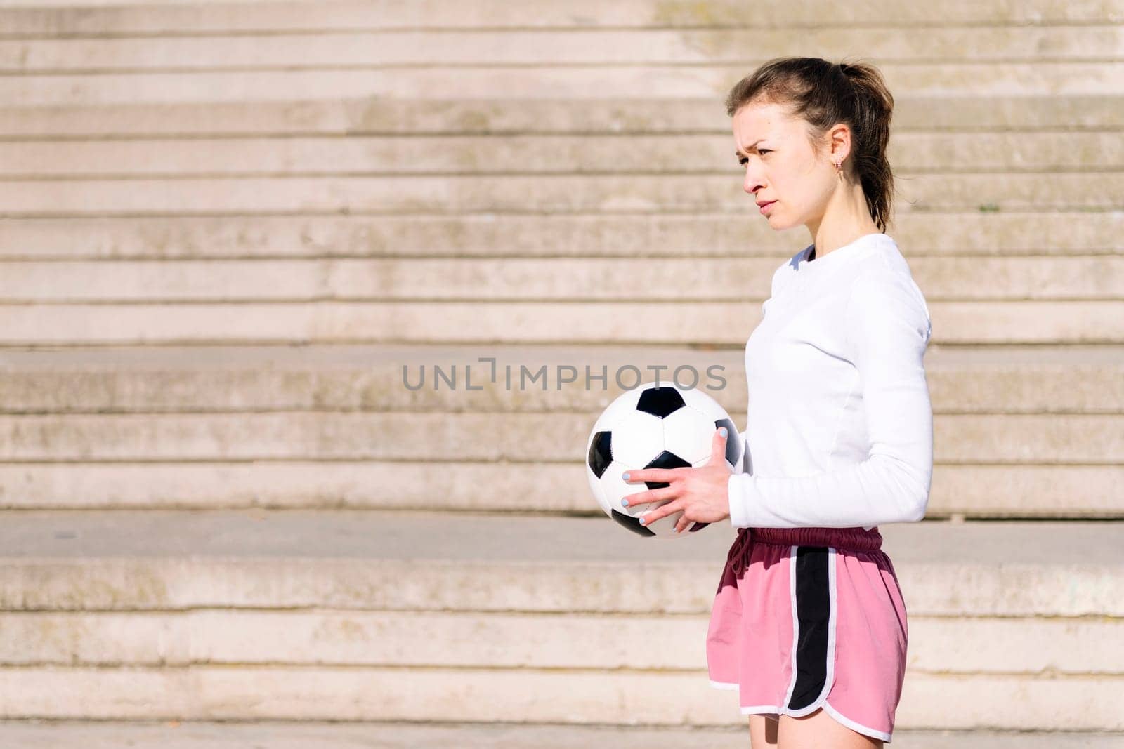 caucasian sports woman standing with the ball in her hand on a concrete soccer court, concept of football lifestyle and urban sport in the city, copy space for text