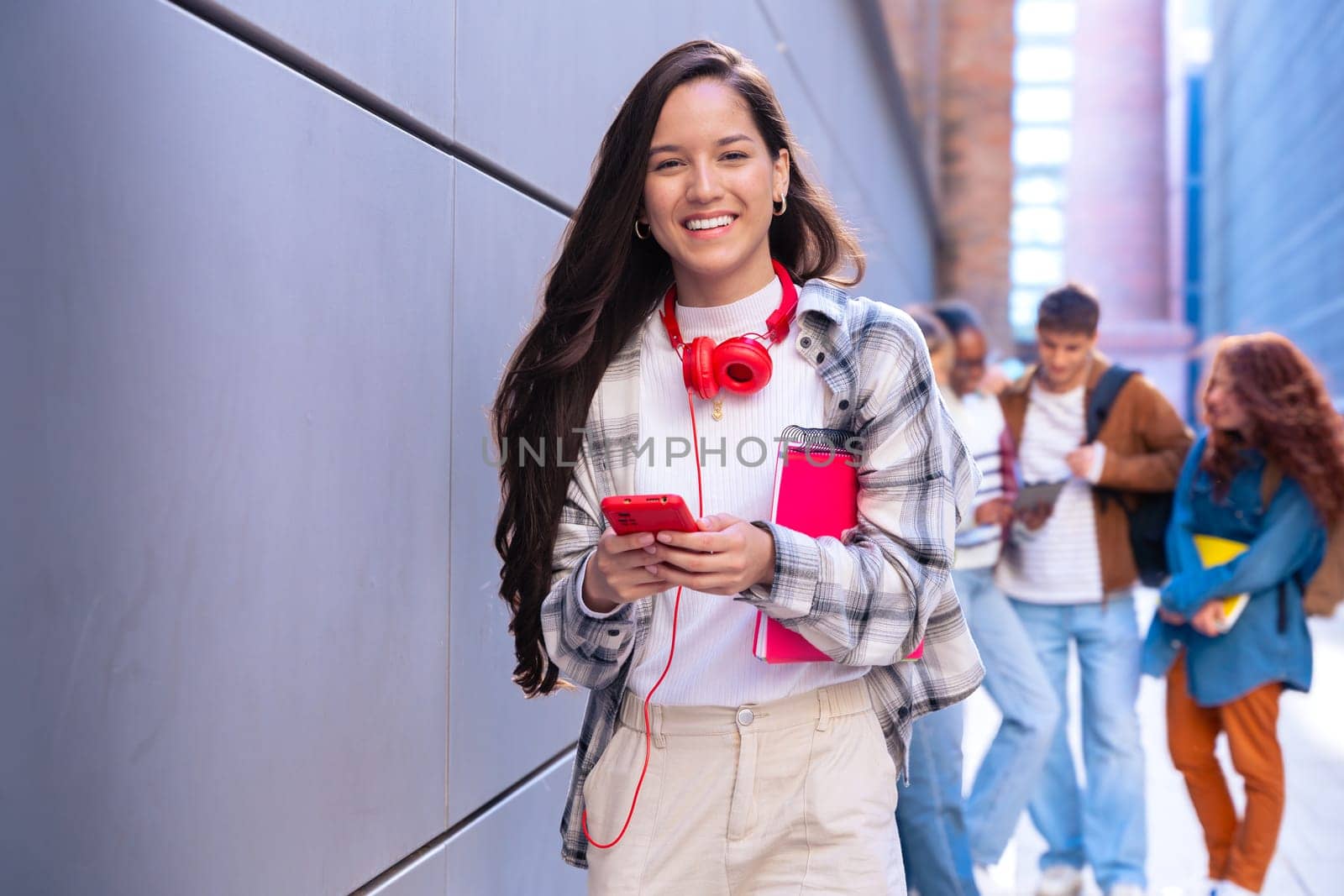 Young smiling student with notebook in hand uses social networks with smartphone applications and wireless technology outdoors.