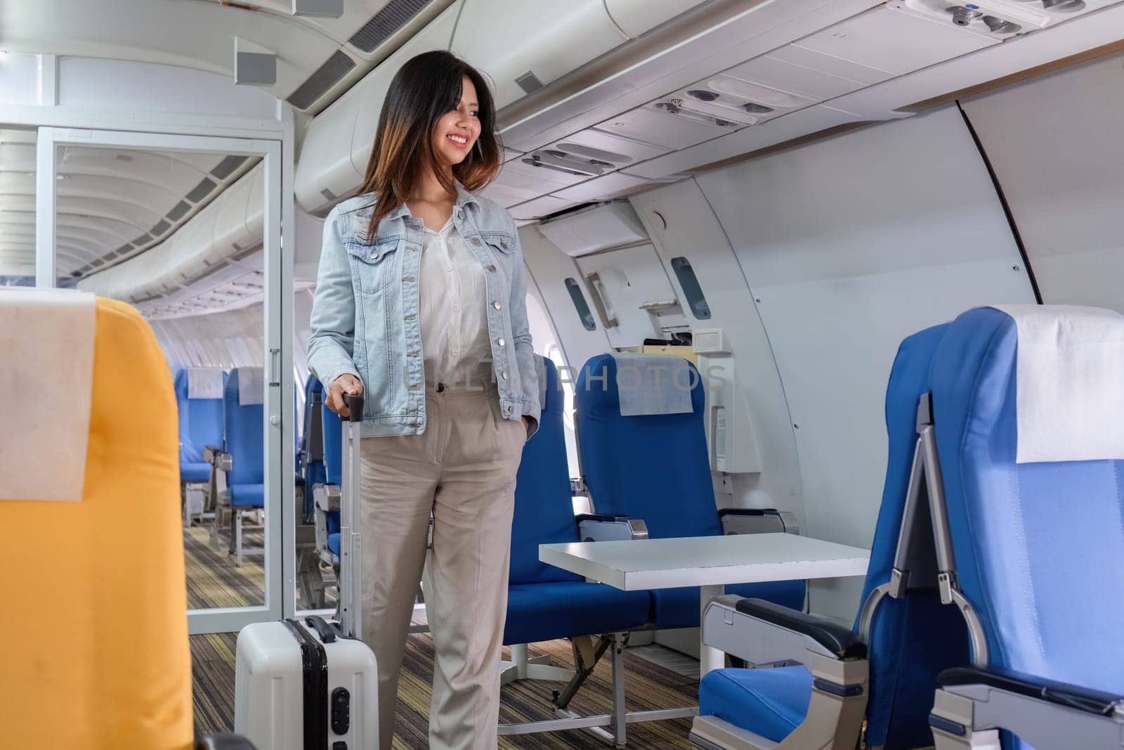 A woman holding a suitcase and traveling by plane, walking through a modern airplane cabin with comfortable seating and a bright interior.