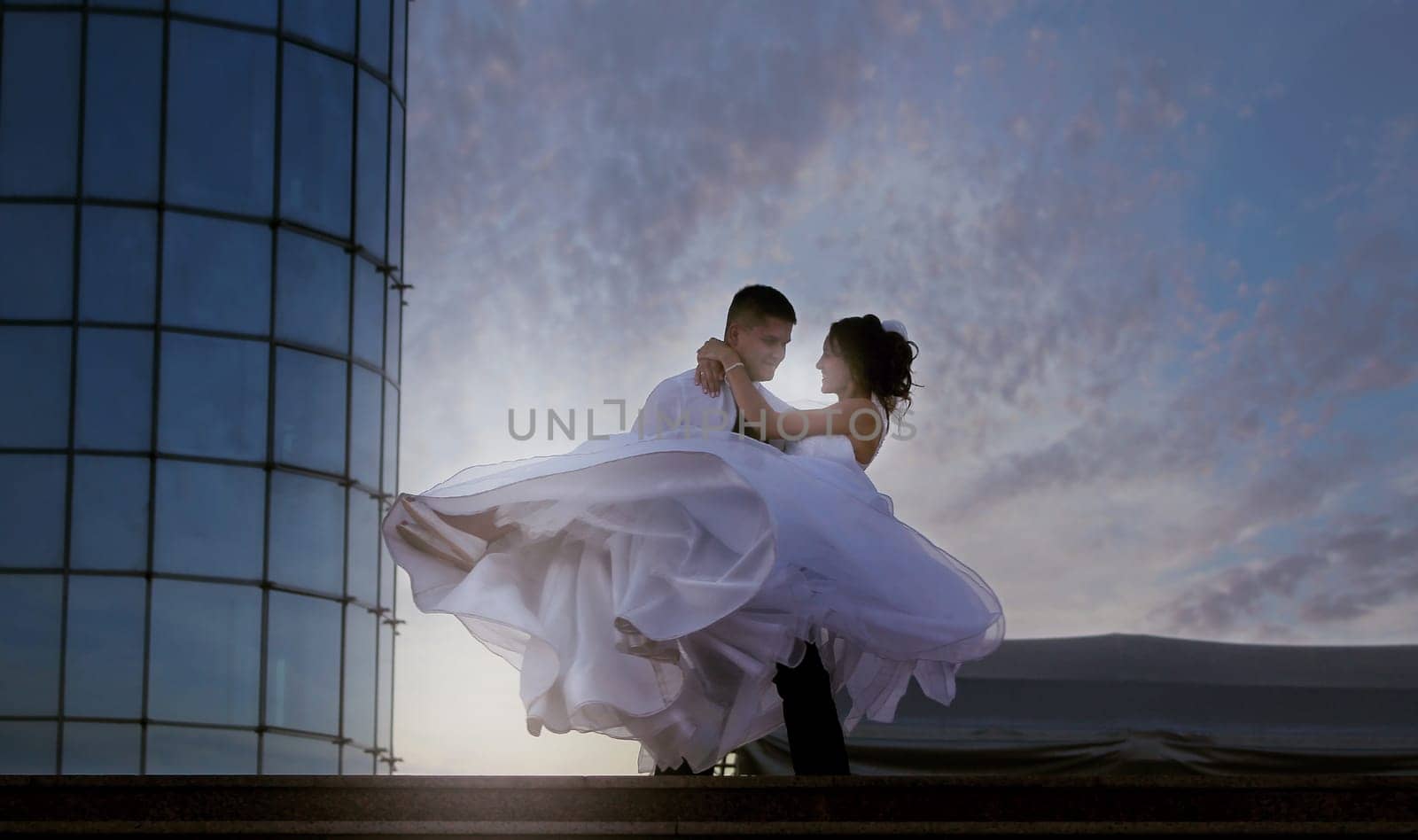 The groom circles his bride against the background of the sunset sky. High quality photo