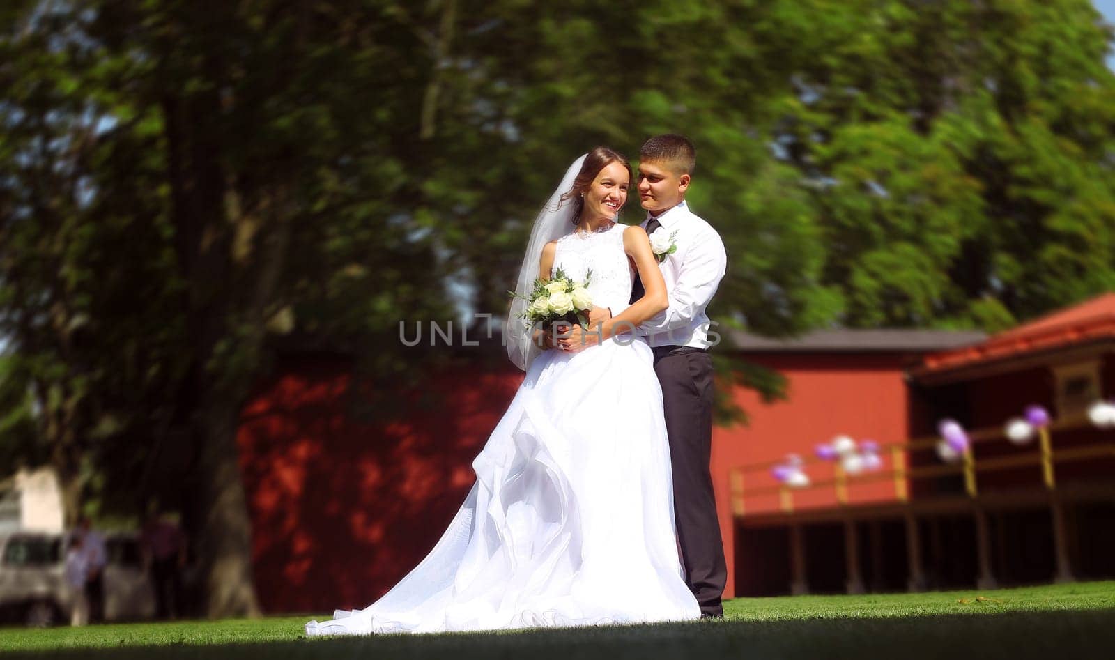 Happy groom hugging his bride holding a bouquet of white roses in her hands. High quality photo
