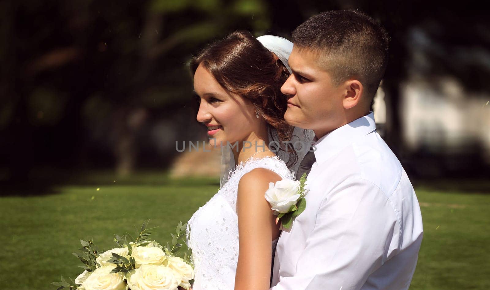 Happy groom hugging his bride holding a bouquet of white roses in her hands. High quality photo