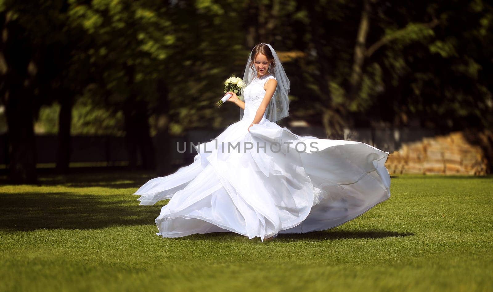 Happy bride in white dress spinning on green lawn by VeronikaAngo