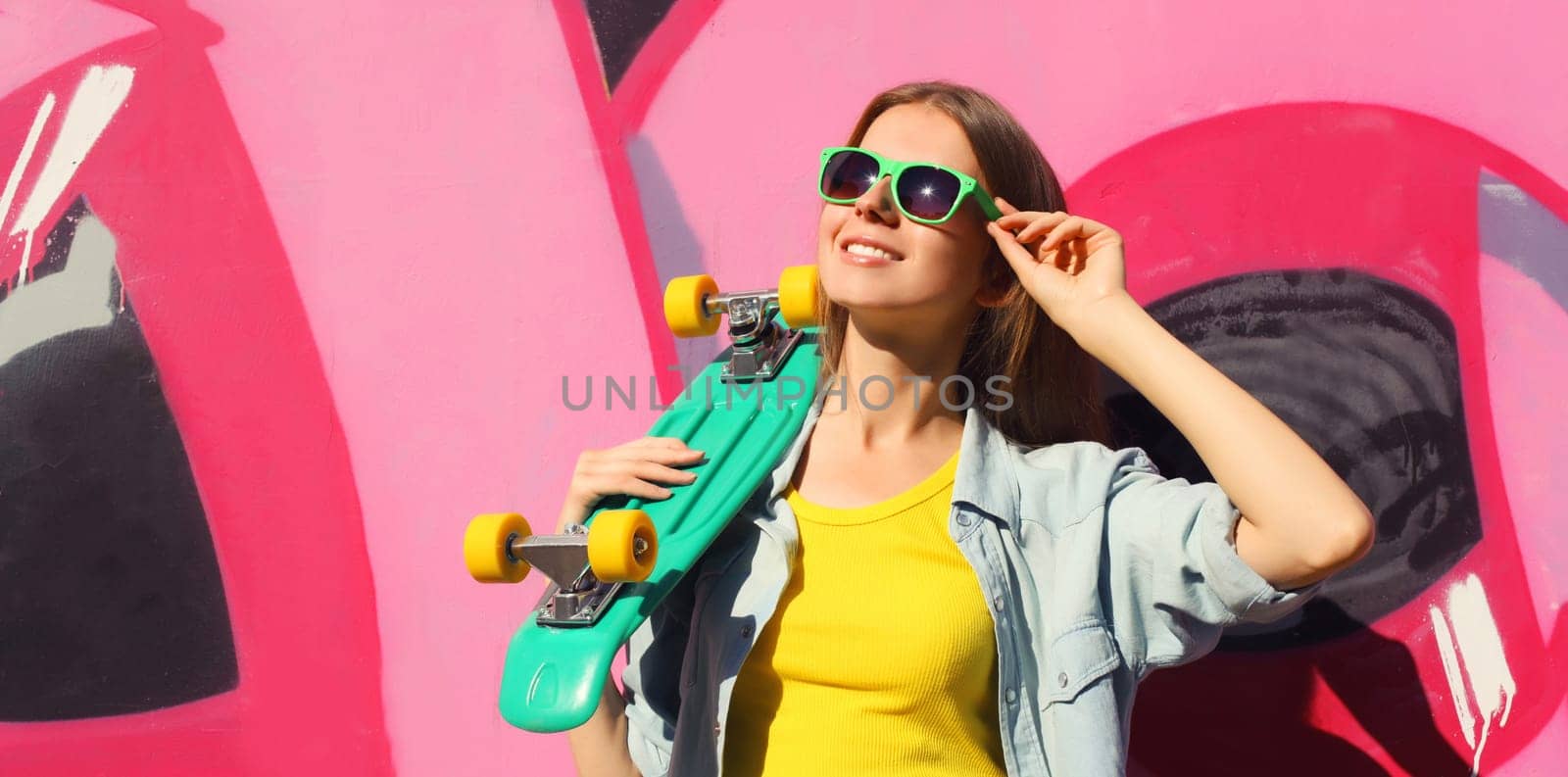 Stylish happy young girl with skateboard in glasses, modern teenager posing against on graffiti wall by Rohappy