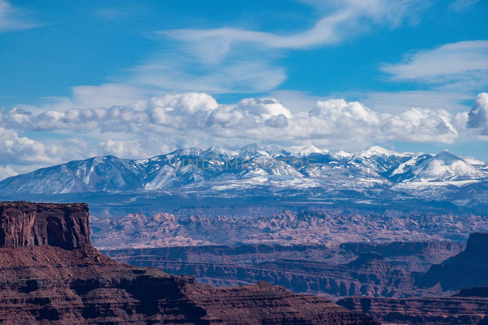 A stunning view of Utah's Canyonlands National Park with the majestic La Sal Mountains in the background. The landscape features rugged canyons and snow-capped peaks - USA