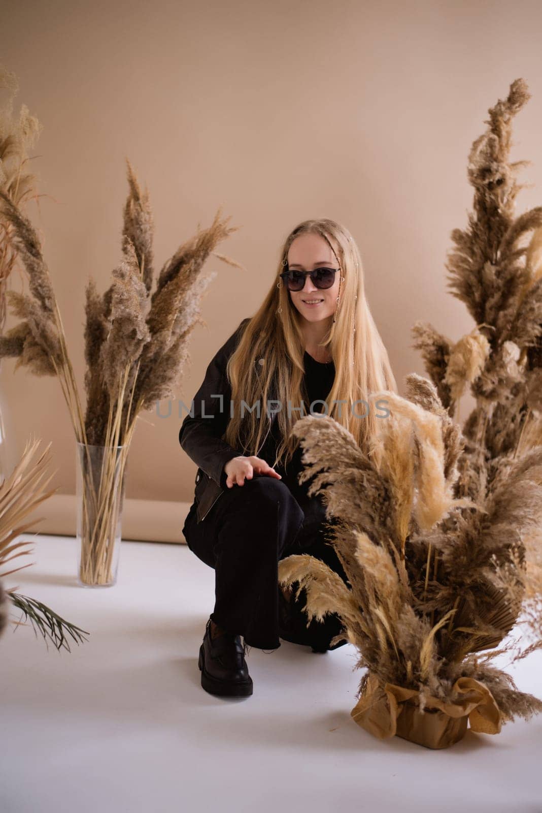 A woman photographer, a blonde with a camera, seriously with sunglasses in the production studio. Wearing a black clothes on a brown background