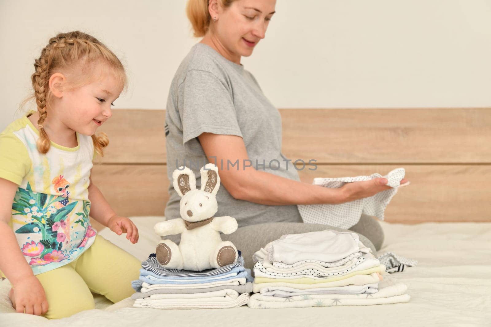 Mother and daughter together prepare clothes for a newborn boy