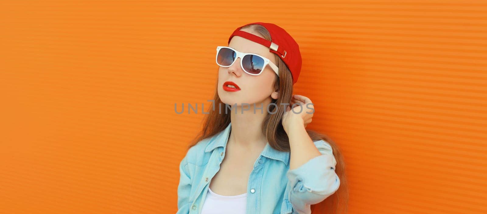 Stylish young girl in baseball cap, glasses, modern teenager girl posing on orange wall background by Rohappy