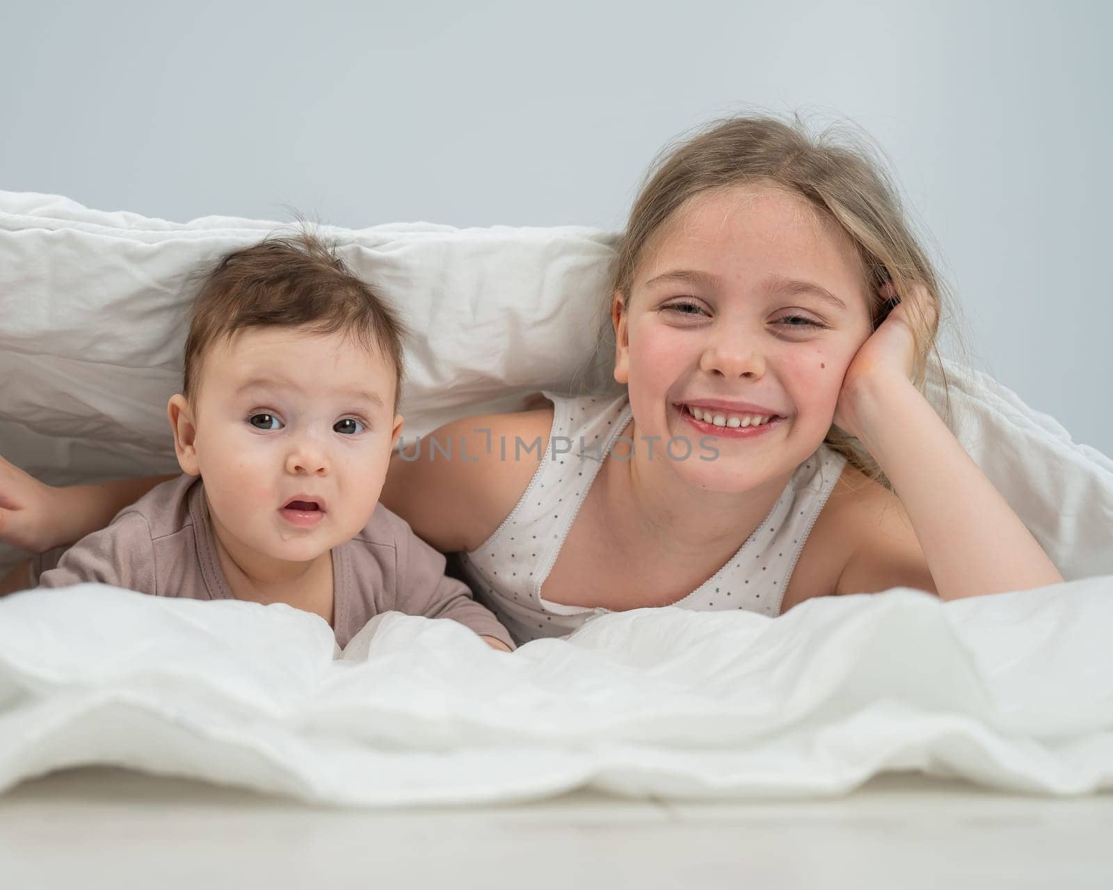 Little girl and her newborn brother hiding under the blanket