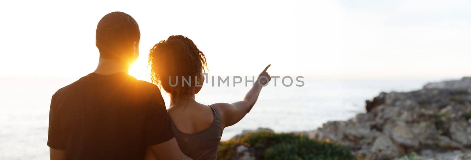 Young african american woman hugging man in sportswear, enjoy workout break, point finger at empty space in morning on rocks at ocean, outdoor. Relationship, health care, active lifestyle and sports