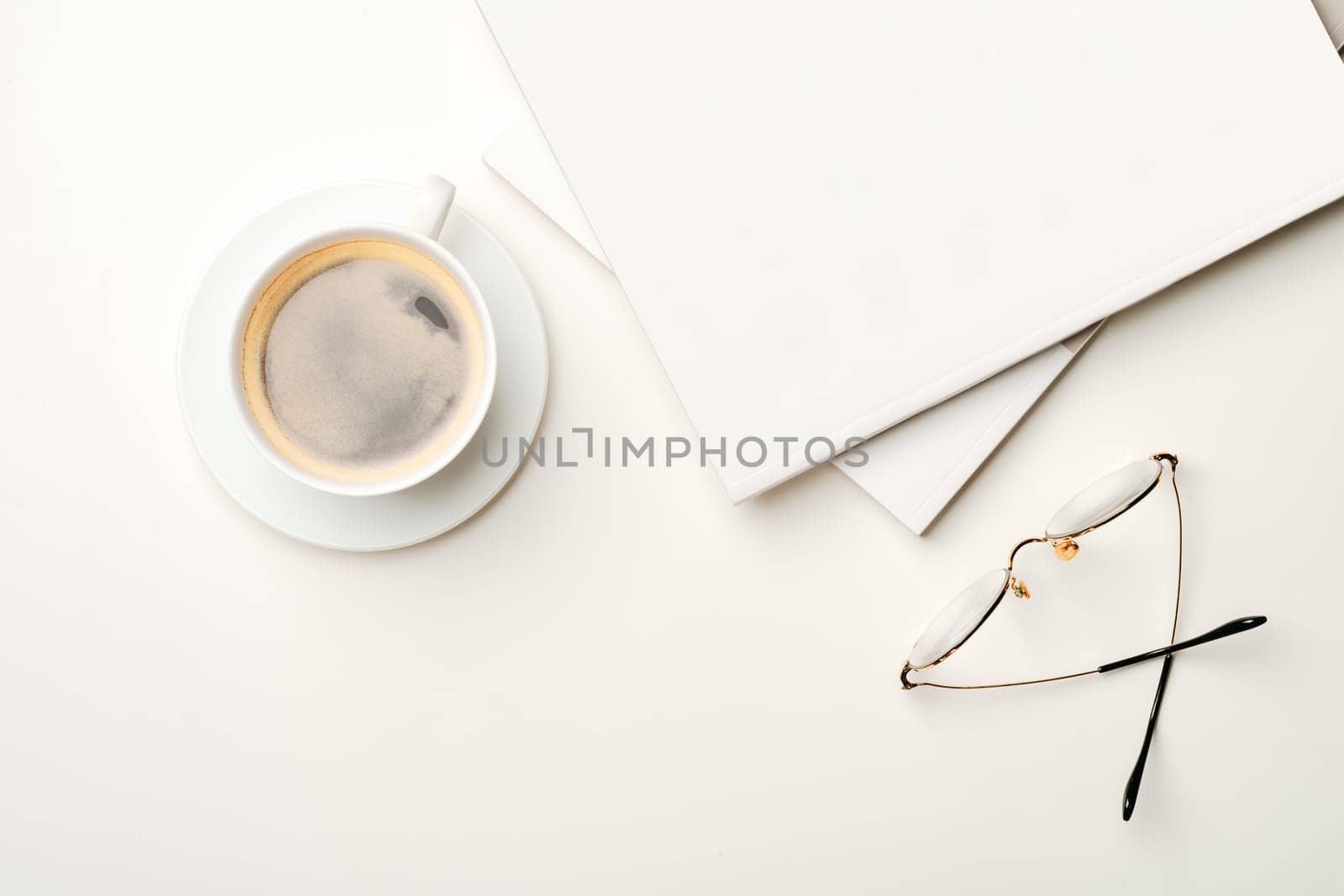 Blank paper, coffee cup and glasses on white desk from above