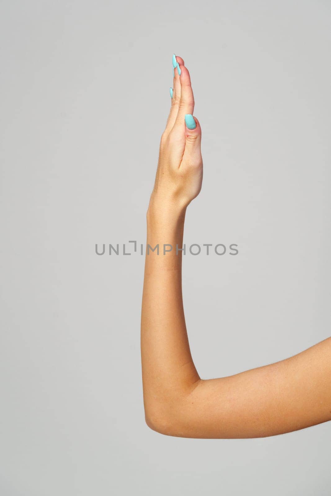 Womans Hand With Blue Nail Polish on gray background close up