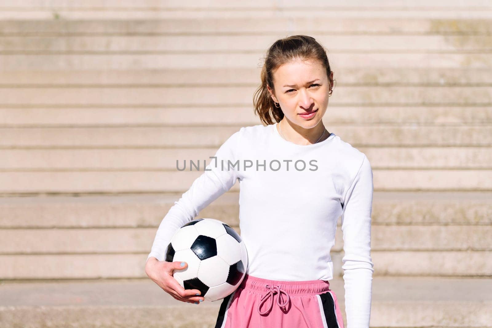 sports woman looking at camera in a concrete soccer court with a ball under her arm, concept of football lifestyle and urban sport in the city, copy space for text