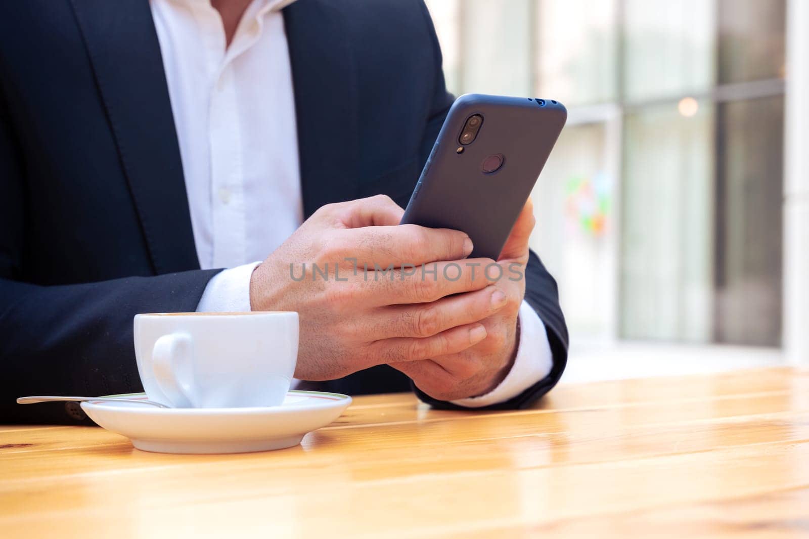 Satisfied with the results, the businessman sitting outside the office building, a mature boss holds a phone and drinks coffee, writes messages and reads news online, using an app.