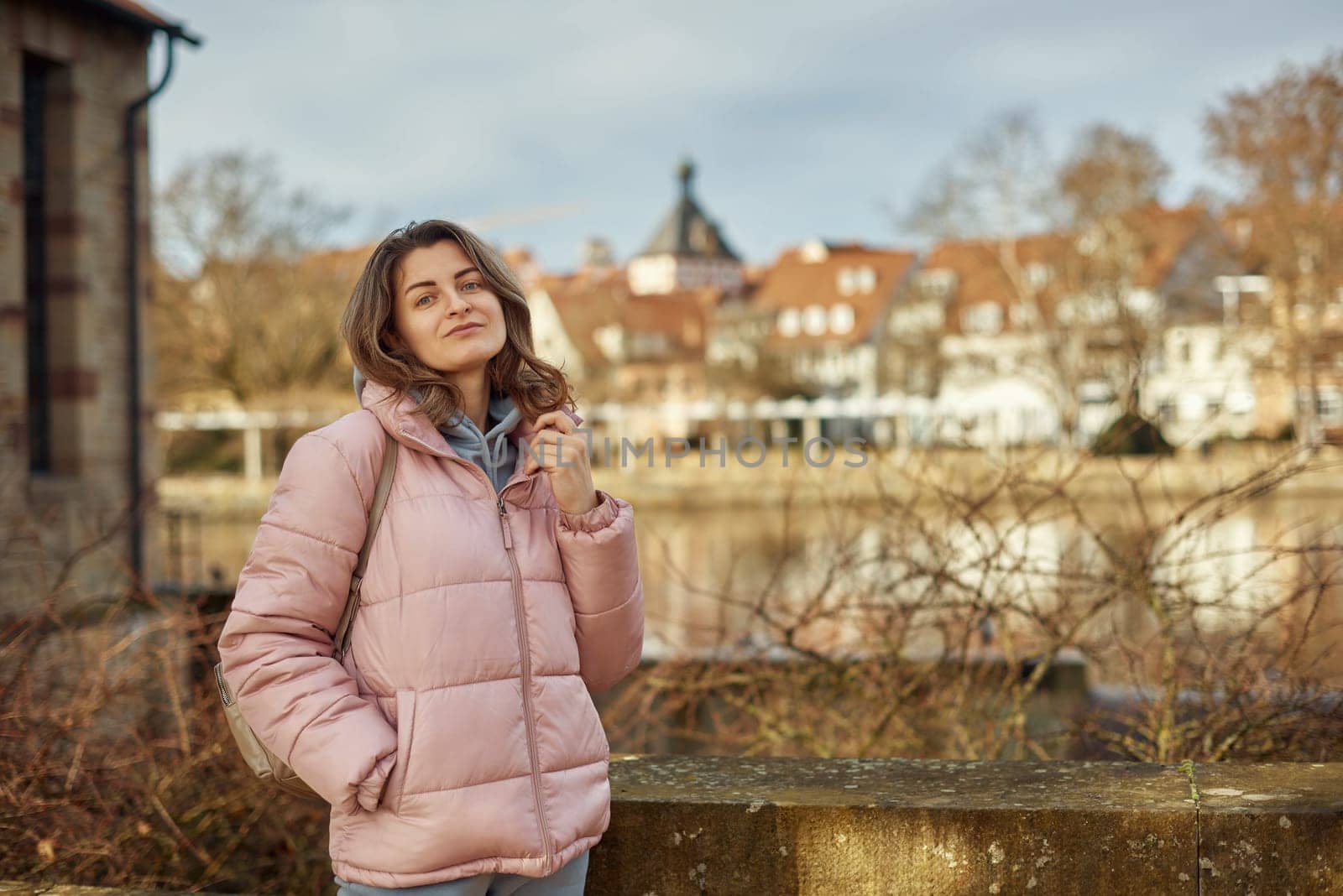 Young beautiful pretty tourist girl in warm hat and coat with backpack walking at cold autumn in Europe city enjoying her travel in Zurich Switzerland. Outdoor portrait of young tourist woman enjoying sightseeing