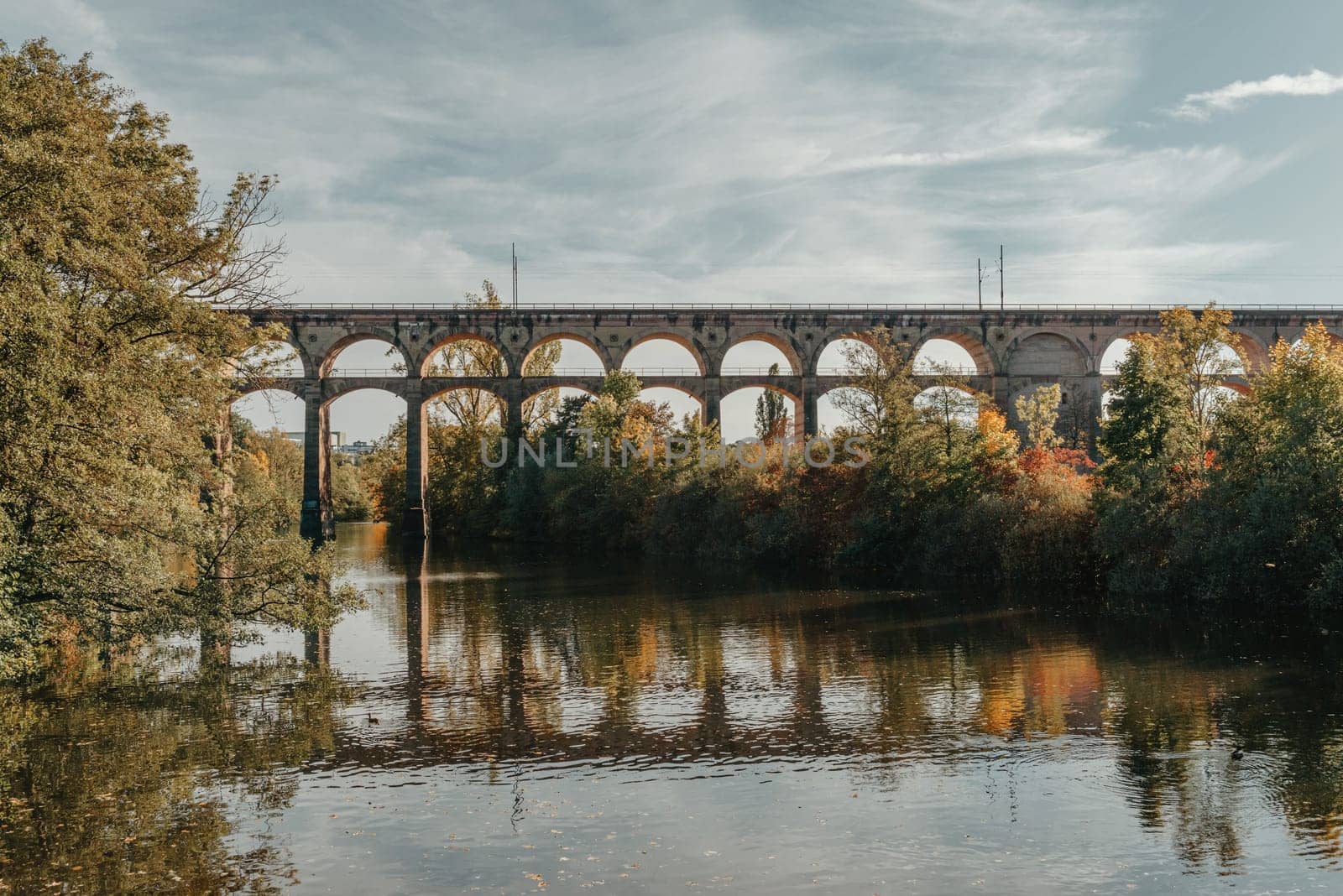 Railway Bridge with river in Bietigheim-Bissingen, Germany. Autumn. Railway viaduct over the Enz River, built in 1853 by Karl von Etzel on a sunny summer day. Bietigheim-Bissingen, Germany. Old viaduct in Bietigheim reflected in the river. Baden-Wurttemberg, Germany. Train passing a train bridge on a cloudy day in Germany by Andrii_Ko